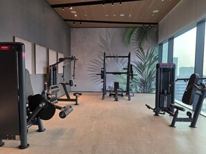 A gym with various exercise machines, a wall with framed artwork, and a large window with a view of palm trees.