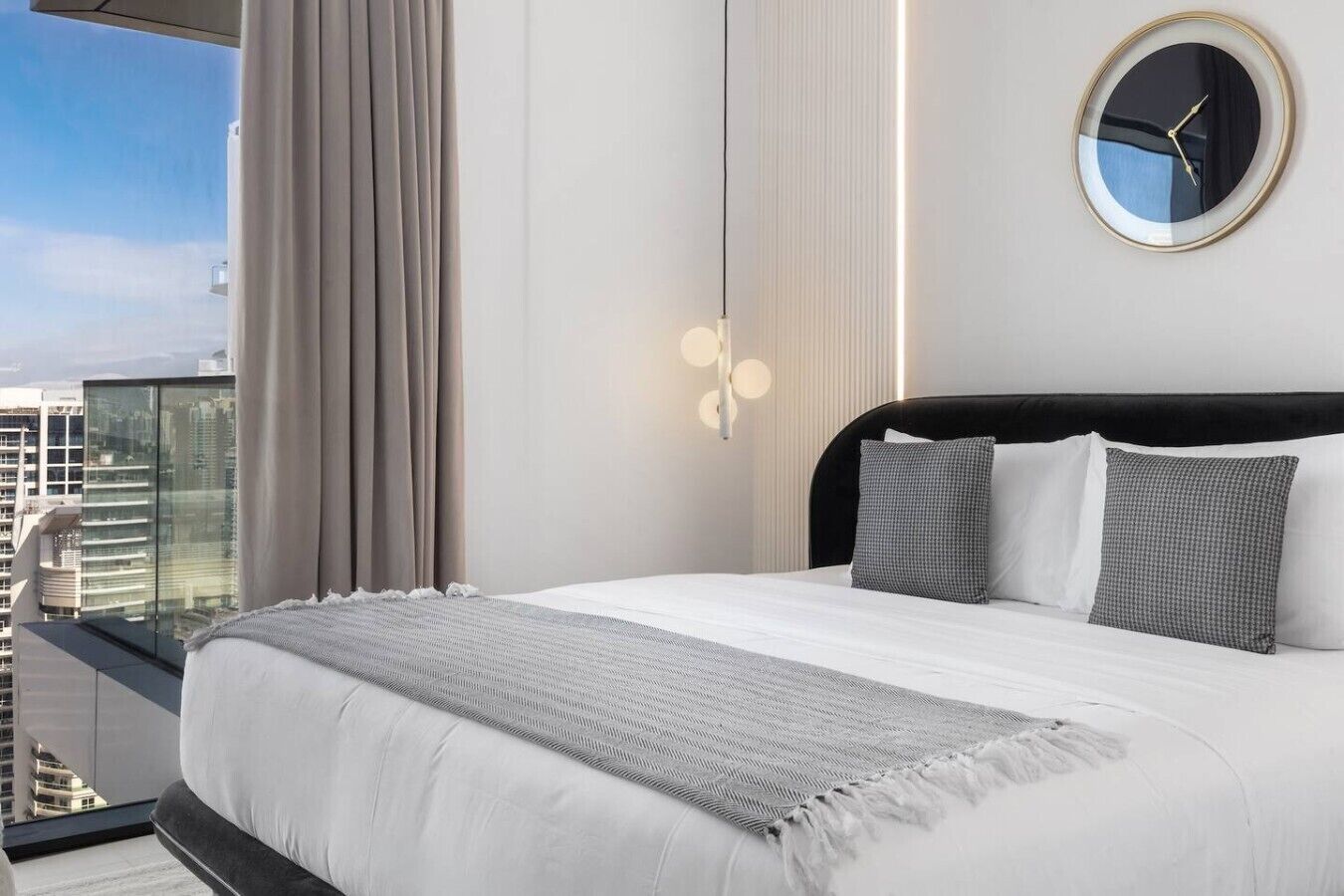 Een moderne hotelkamer met een groot bed, uitzicht op de stad en een ronde wandklok.