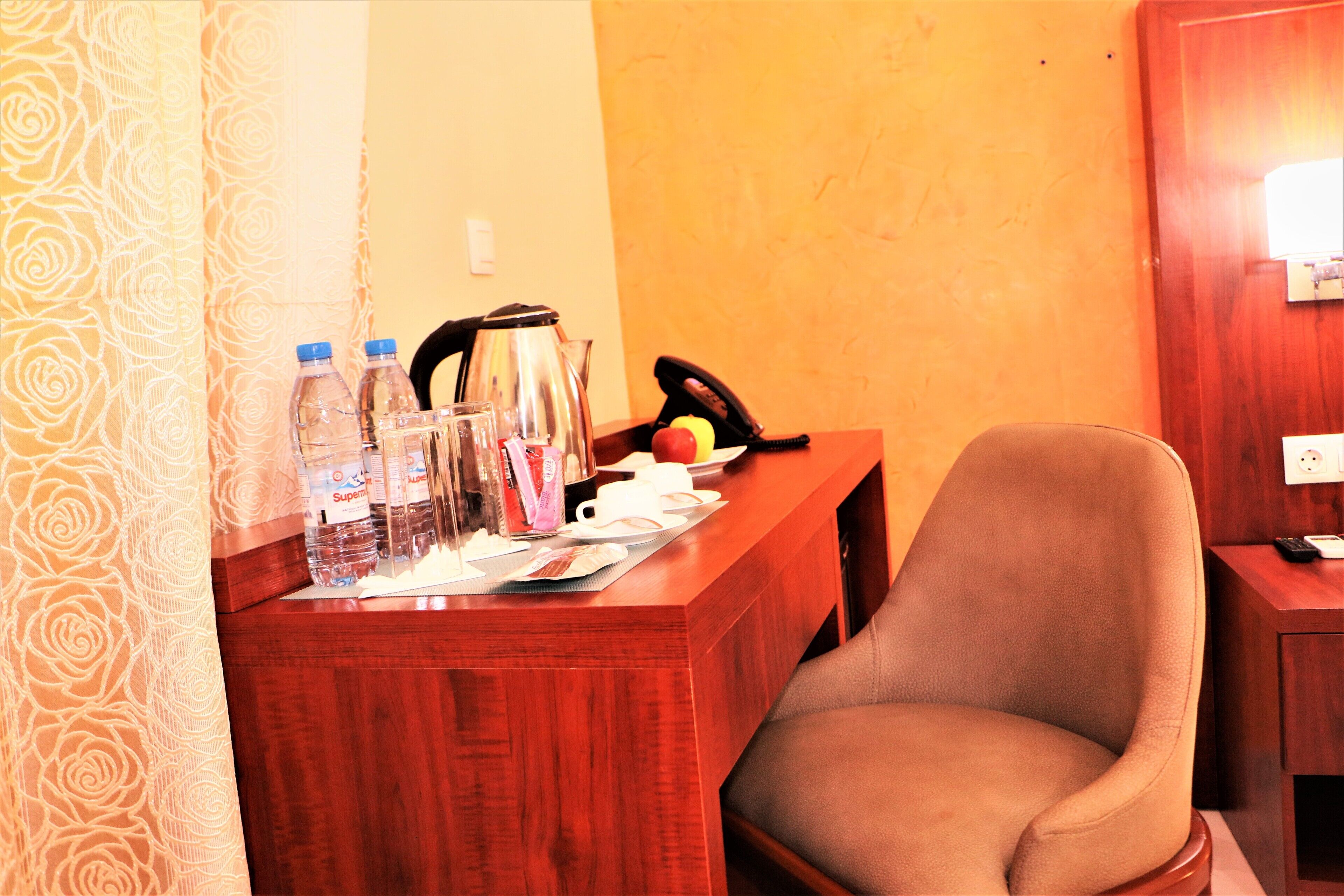 A wooden desk with a chair, a kettle, a telephone, and various items including bottles and cups.