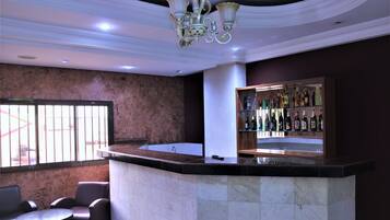 Zona de bar con mostrador de mármol, asientos y una estantería repleta de licores.