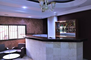 Zona de bar con mostrador de mármol, asientos y una estantería repleta de licores.