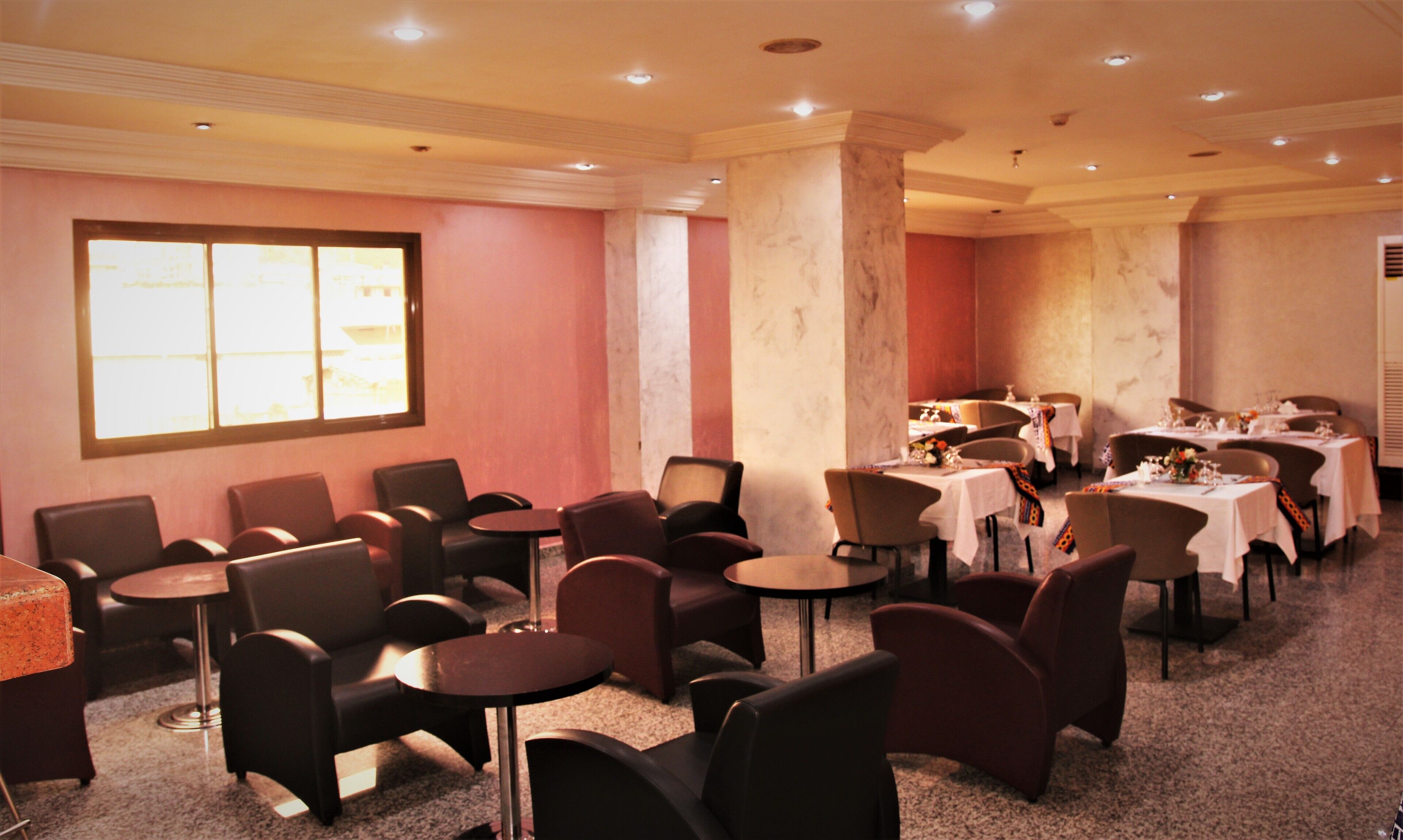 A hotel dining area with multiple tables and chairs, a large window, and marble columns.