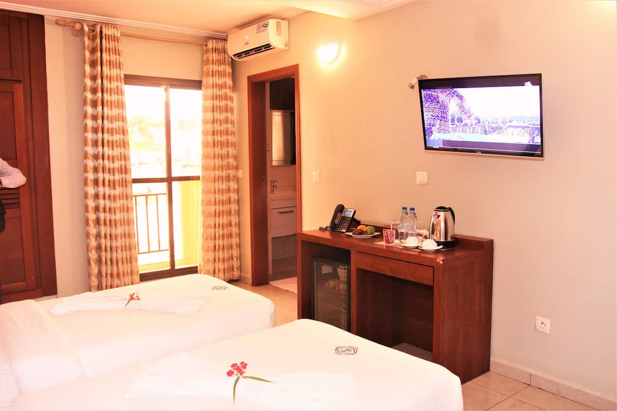A hotel room with two beds, a desk with a telephone and a kettle, a television, and a window with curtains.