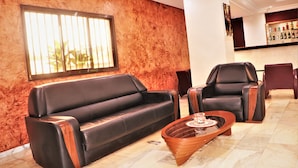 A lobby with a leather sofa, two leather armchairs, a wooden coffee table, and a bar area with various bottles. - Jouvence International Hôtel (Yaoundé)
