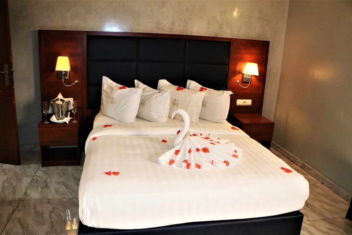 A neatly made bed with a swan design on the bedspread, flanked by two bedside tables with lamps, and a dark headboard.