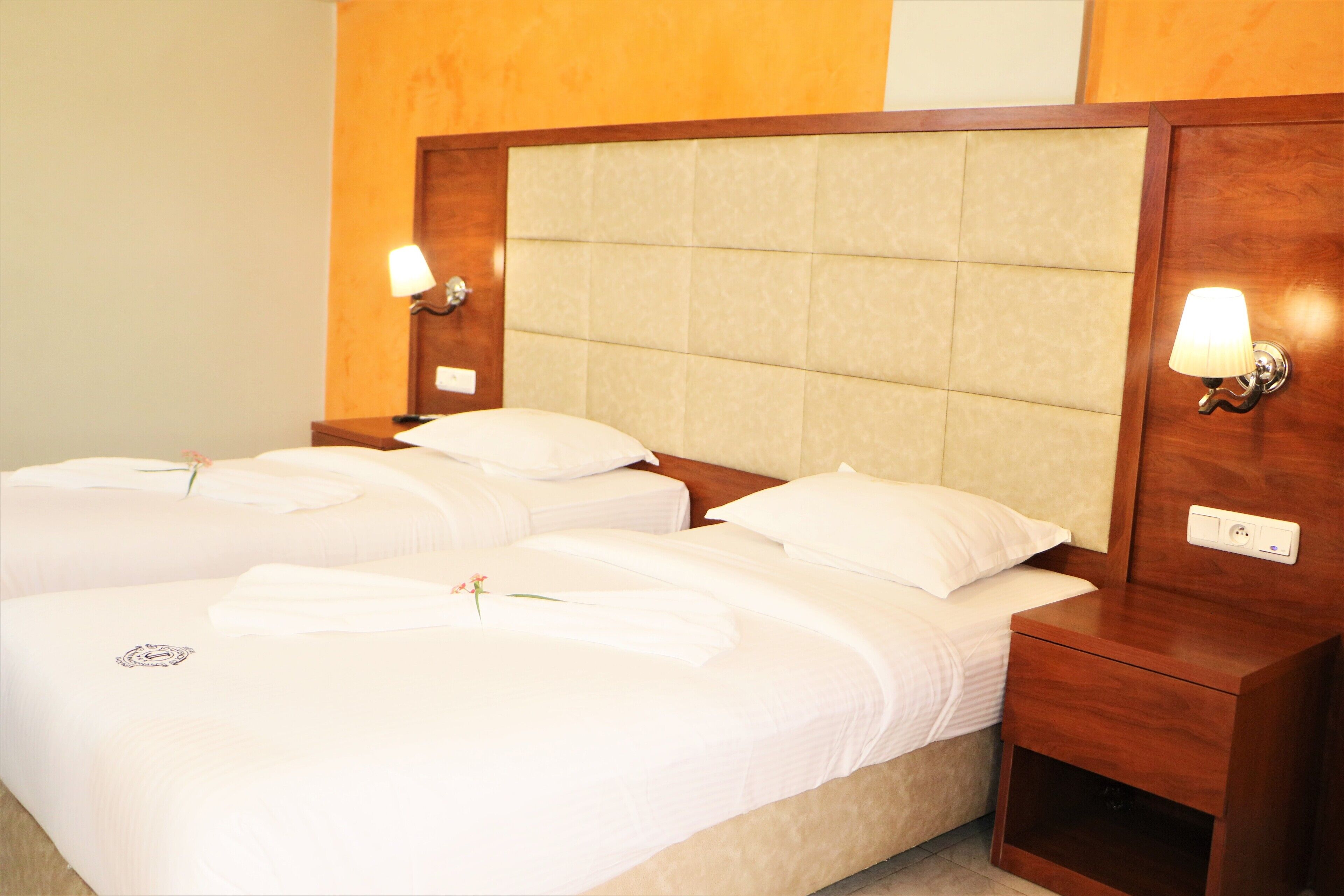 A hotel room with two beds, each with white linens and pillows, a wooden headboard, and bedside lamps.