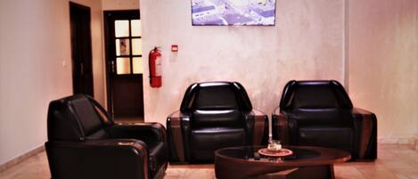 A lobby with three leather chairs, a coffee table, a fire extinguisher, and a television mounted on the wall.