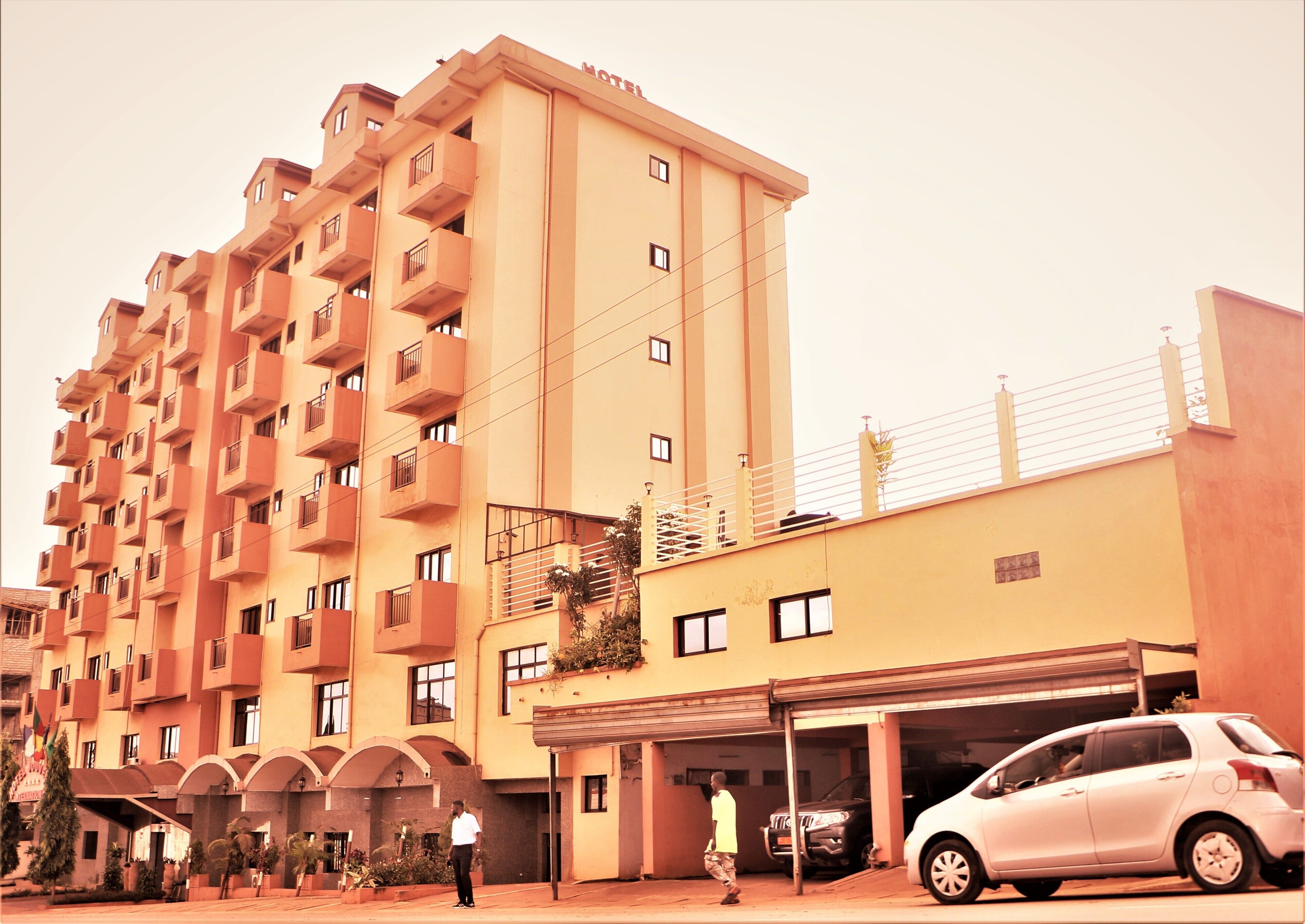 A multi-story hotel with balconies, a parking area, and a covered entrance.