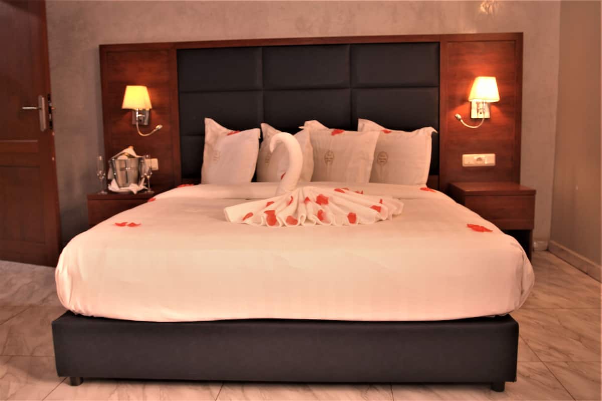 A neatly made bed with a large pillow arrangement in the center, two bedside tables with lamps, and a dark headboard.
