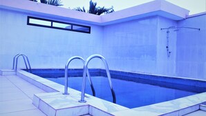 A swimming pool with two ladders, a shower area, and a tiled wall. - Jouvence International Hôtel (Yaoundé)