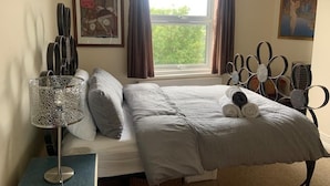 A bedroom with a bed, a bedside table with a lamp, a window with curtains, and a wall with a tennis racket decoration. - Apartmentsleeps2-seaside Escape-wifi-parking (Hastings)