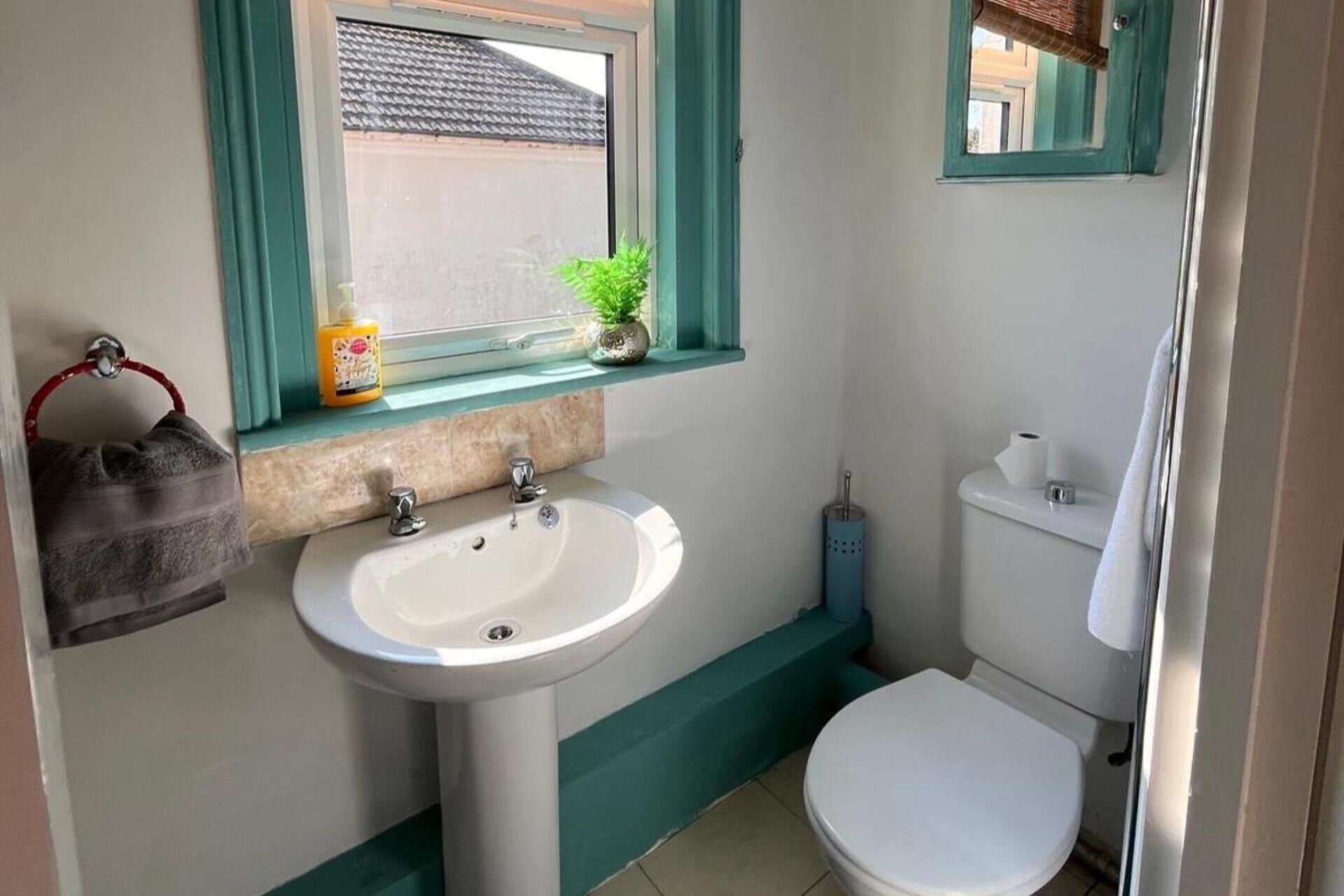 A bathroom with a white sink, a toilet, and a window with a view of the outside.