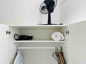 A white wardrobe with a fan on top, a folded towel, and a black bag on the shelf. - Private Rooms Sleeps 7 With Wi-fi (London)