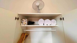 Ein Badezimmer mit einem weißen Ventilator auf einem Regal, einem Handtuchhalter darunter und einer Aufbewahrungseinheit für Handtücher, inklusive Handtücher und einer verzierten Schachtel.