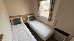 Una habitación pequeña y acogedora con dos camas individuales, una ventana con cortinas y un radiador.