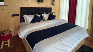 A bed with a dark blue and white bedspread, a wooden headboard, and a small stool with a red cushion.