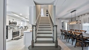 A modern kitchen with stainless steel appliances, a dining area with a wooden table and chairs, and a staircase with a unique design. - Pool, Game Room, 3 Kings | Magnolia Beach House (Cocoa Beach)