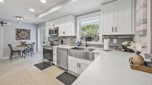 A modern kitchen with white cabinetry, stainless steel appliances, and a dining area with a table and chairs. - Pool, Game Room, 3 Kings | Magnolia Beach House (Cocoa Beach)
