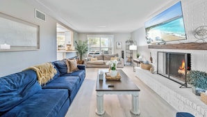 A living room with a blue sofa, a fireplace, a TV, and a view of the beach. - Pool, Game Room, 3 Kings | Magnolia Beach House (Cocoa Beach)