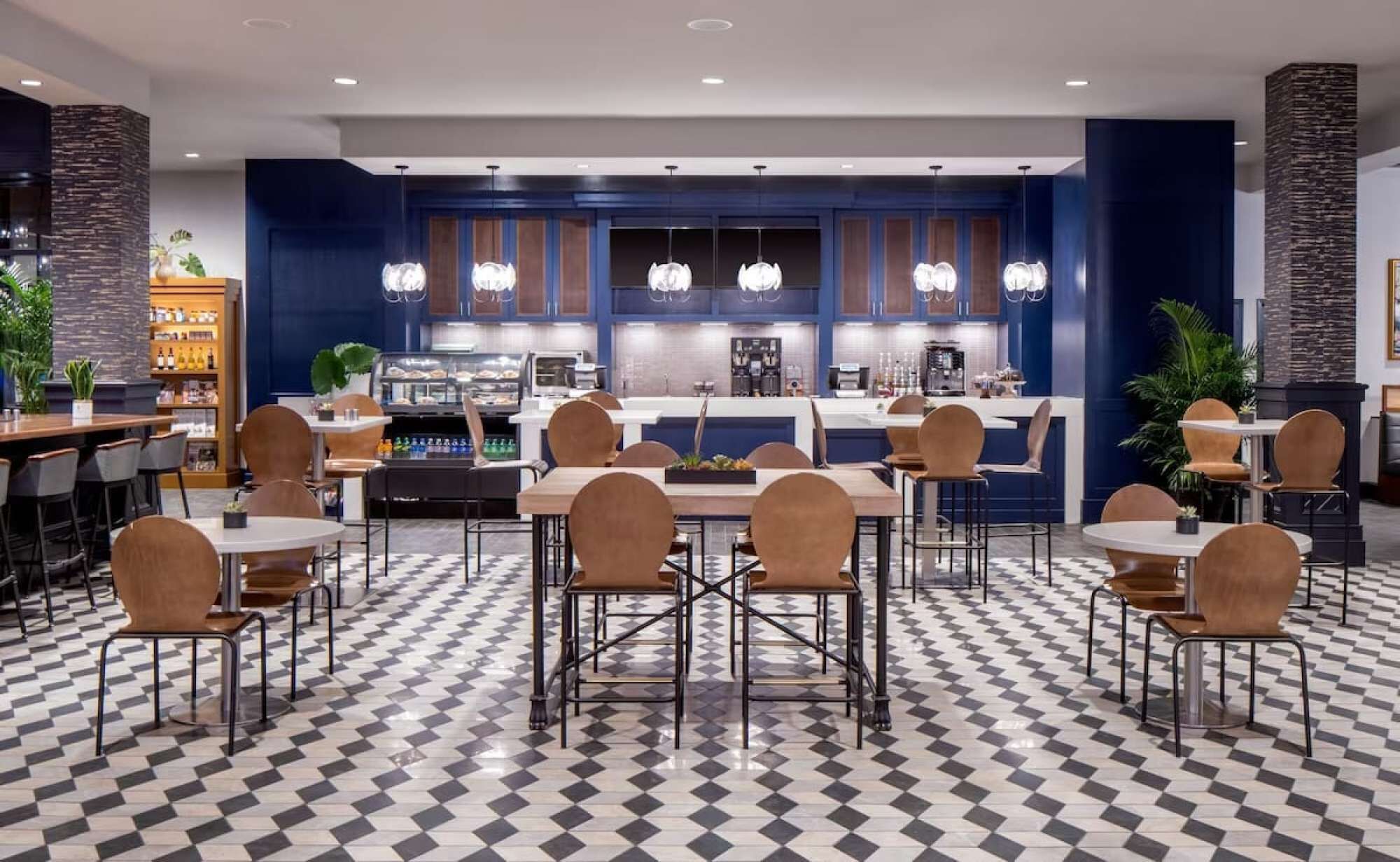 Un hall d’hôtel moderne avec un sol à carreaux, un bar central et des espaces aménagés pour s’asseoir.