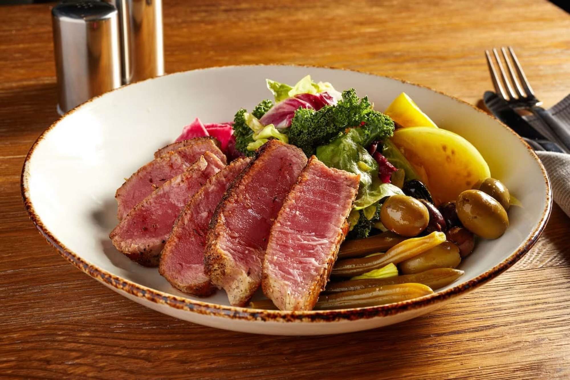 Une assiette de nourriture contenant des tranches de viande, des légumes et des pommes de terre.