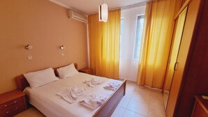 Une chambre d’hôtel équipée d’un lit, de tables de chevet, d’un climatiseur, d’une armoire et d’une fenêtre avec des rideaux.