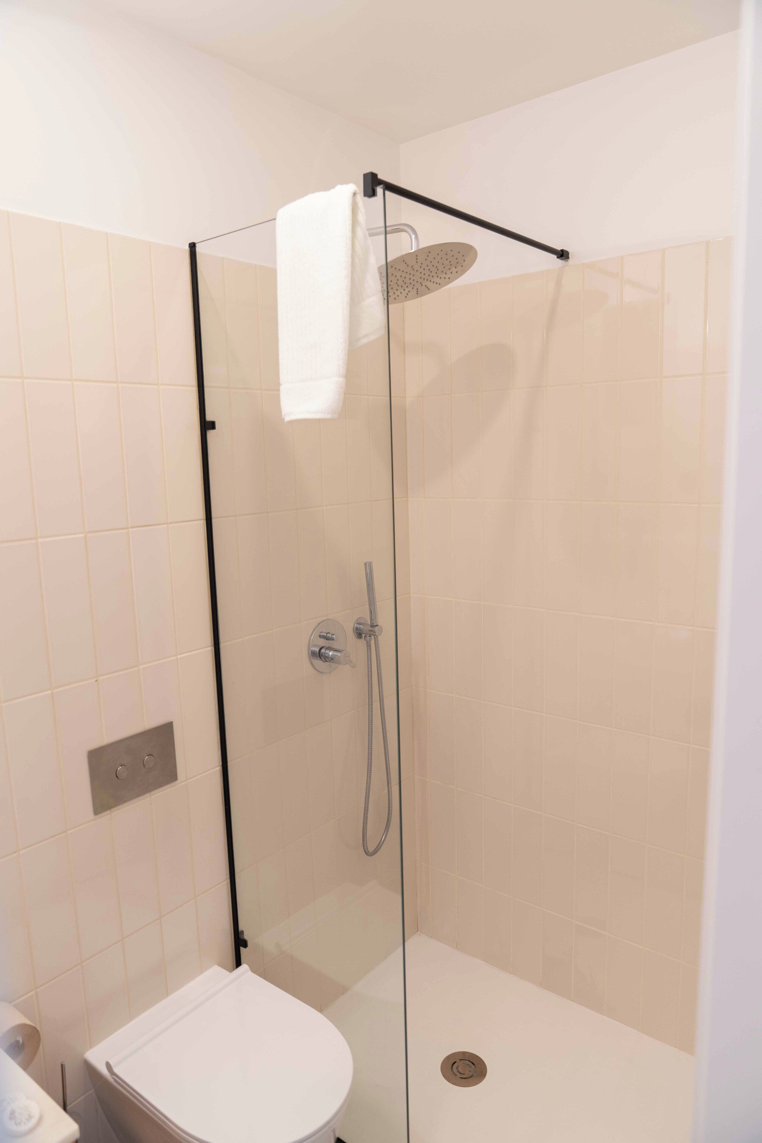 Een douchecabine met glazen wanden, een wit toilet en een handdoekhouder.