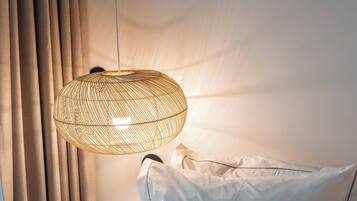 A bed with white bedding and a woven light fixture above it.