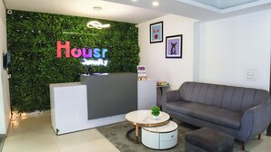 Un espace d’accueil agrémenté d’un mur végétal, d’un comptoir de réception, d’un canapé gris et d’une petite table ronde sur laquelle est posée une plante.