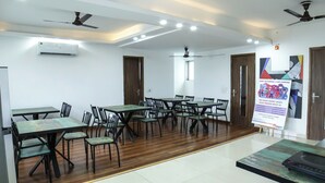 Une salle de conférence équipée de plusieurs tables et chaises, de ventilateurs de plafond et d’un appareil de climatisation.