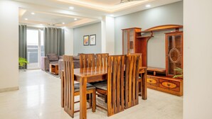 A dining area with a wooden table and chairs, a sofa, and a cabinet with decorative elements. - Housr 3 BHK Apartment Sector 45 Gurgaon (Gurugram)