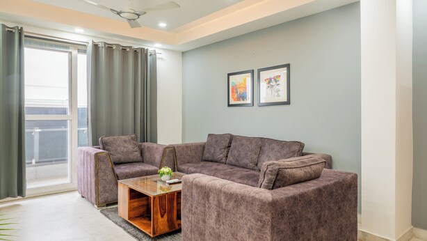 A modern living room with a grey sofa set, a wooden coffee table, and a ceiling fan. - Housr 3 BHK Apartment Sector 45 Gurgaon (Gurugram)
