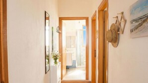 A hallway with a wooden floor, a rug, a mirror, and a door leading to a bathroom.