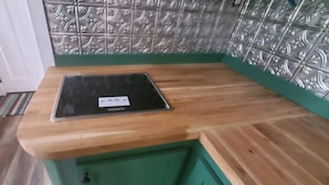 A kitchen with a wooden countertop, a green sink, and a decorative backsplash.