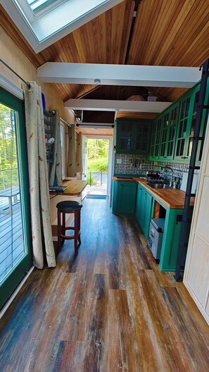 Een keuken met houten vloeren, groene kastjes en een raam met gordijnen.