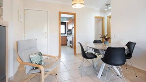 Ein modernes Wohnzimmer mit Essbereich, einer Küche im Hintergrund und einem großen Fenster.