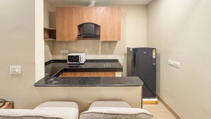A compact kitchenette with a microwave, a black refrigerator, wooden cabinets, and a small countertop. - Housr 1 BHK Apartment Sector 42 Gurgaon (Gurugram)