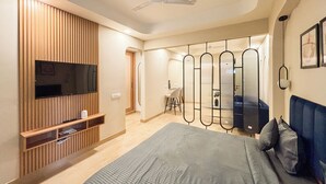A modern bedroom with a large bed, a TV mounted on a wooden panel wall, a ceiling fan, and a walk-in closet with mirrors. - Housr 1 BHK Apartment Sector 42 Gurgaon (Gurugram)