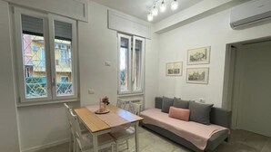 Uma sala de estar moderna com sofá, uma mesa de jantar com cadeiras e uma janela com persianas.