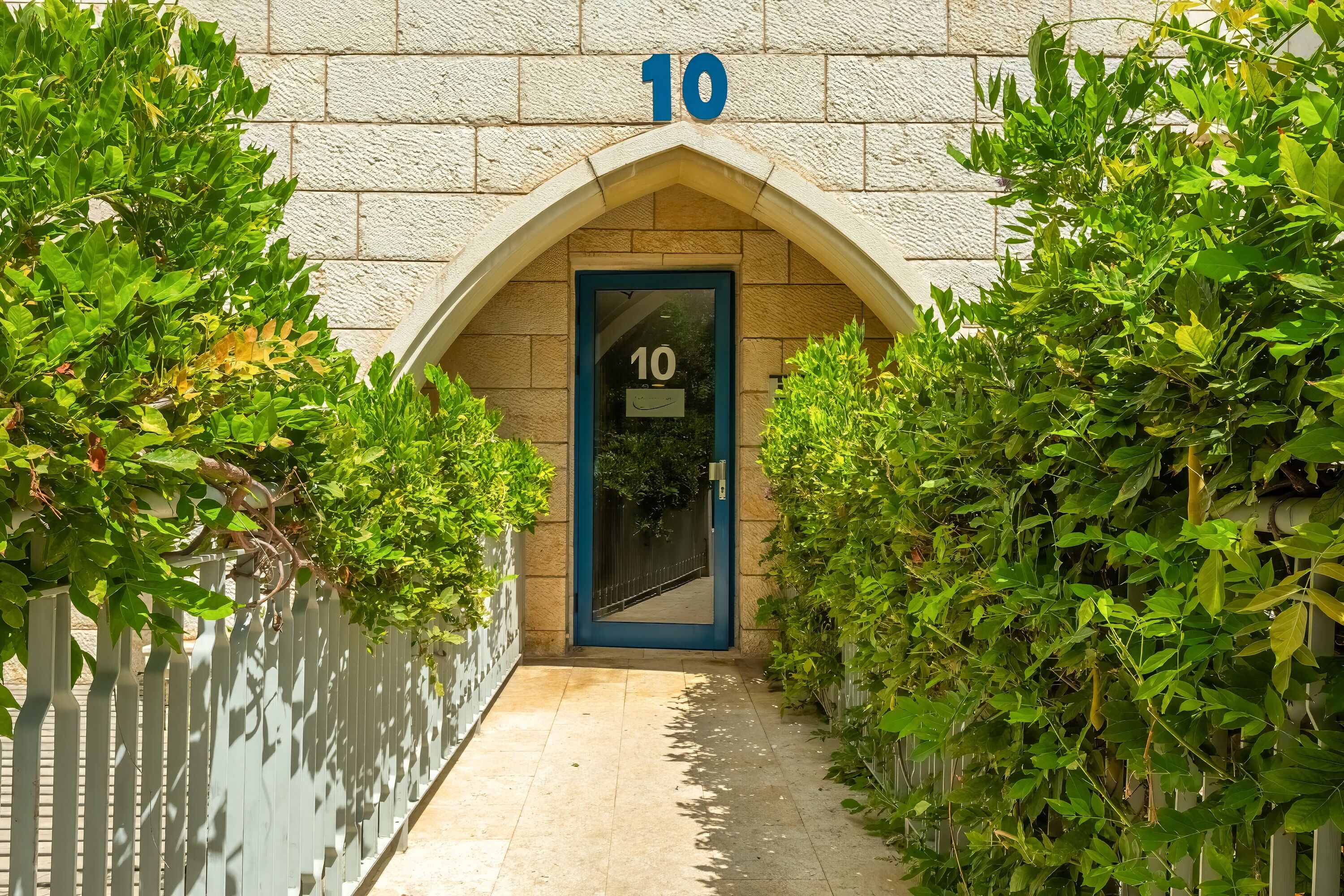 Une entrée d’immeuble avec une plaque portant le numéro 10 au-dessus d’une porte, le tout entouré de verdure.