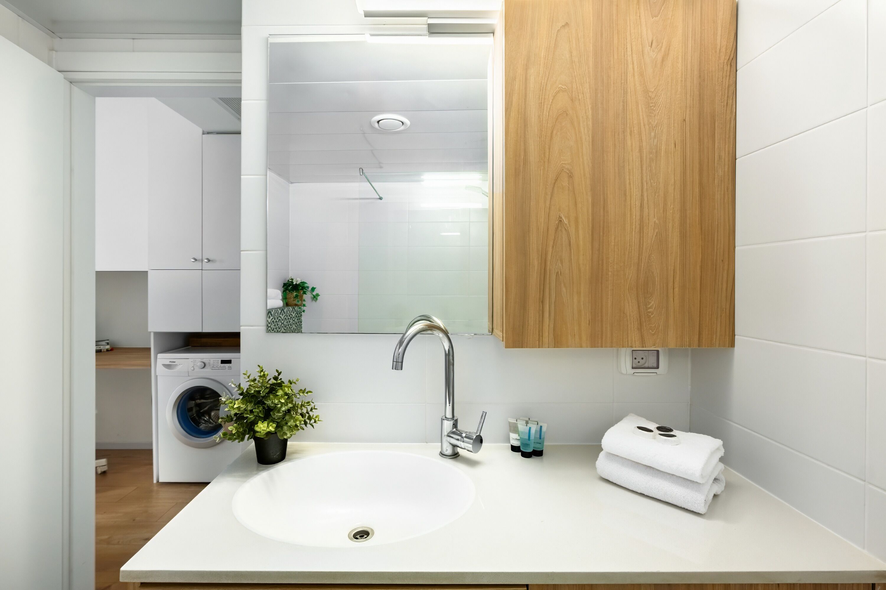 A modern bathroom with a white sink, a wooden cabinet, and a mirror above the sink.