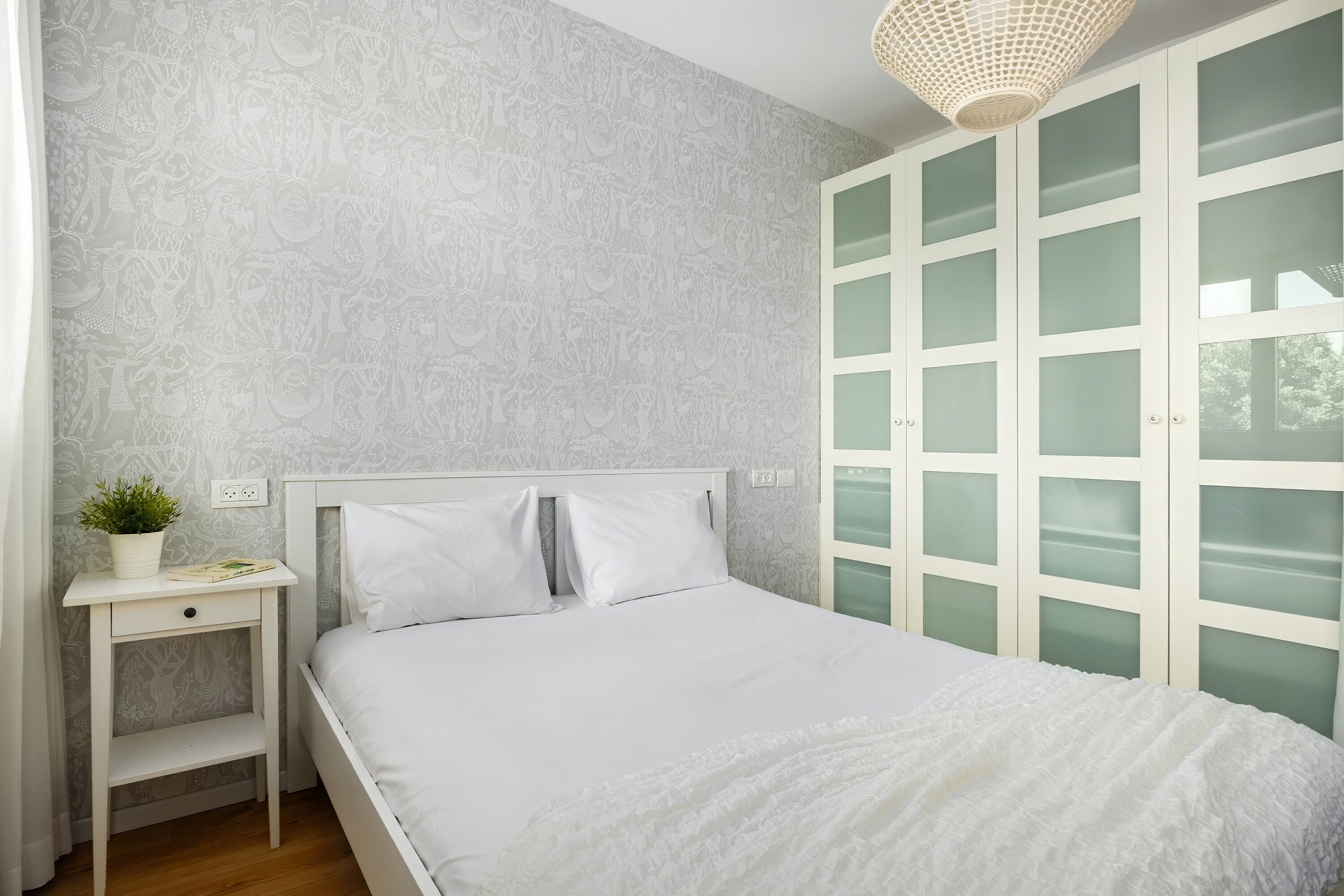 A bedroom with a bed, a nightstand, a potted plant, and a wardrobe with frosted glass doors.