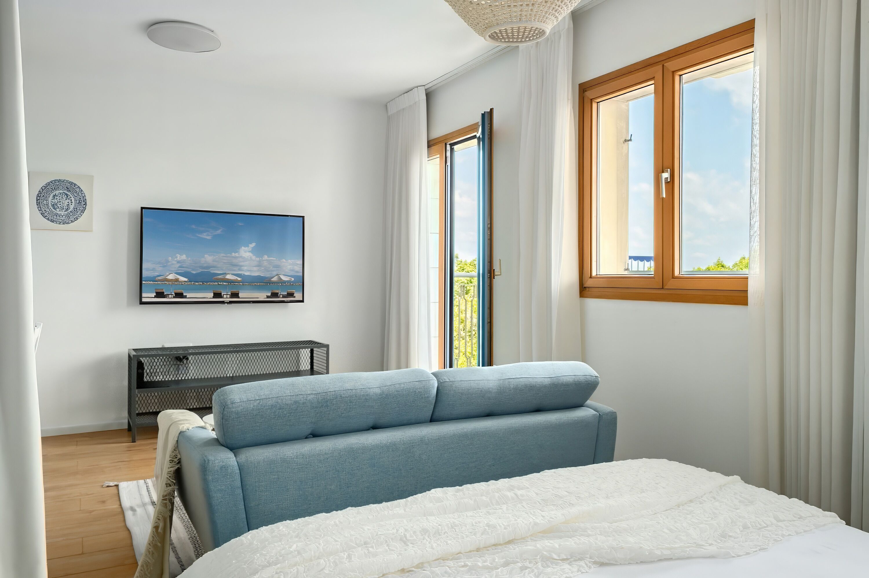 Ein Schlafzimmer mit einem Bett, einem blauen Sofa, einem an der Wand montierten Fernseher und einem großen Fenster mit Vorhängen.