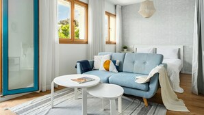 Quarto moderno com sofá azul, cama branca e uma grande janela.