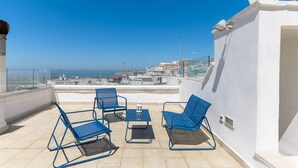 Una terraza en la azotea con cuatro sillas azules, una mesa pequeña y una antena parabólica blanca.