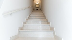 Una escalera con paredes blancas y barandilla, que conduce a un rellano con una lámpara.