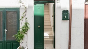 Un pasillo estrecho con una puerta verde, una planta en maceta y una escalera que sube a un piso superior.