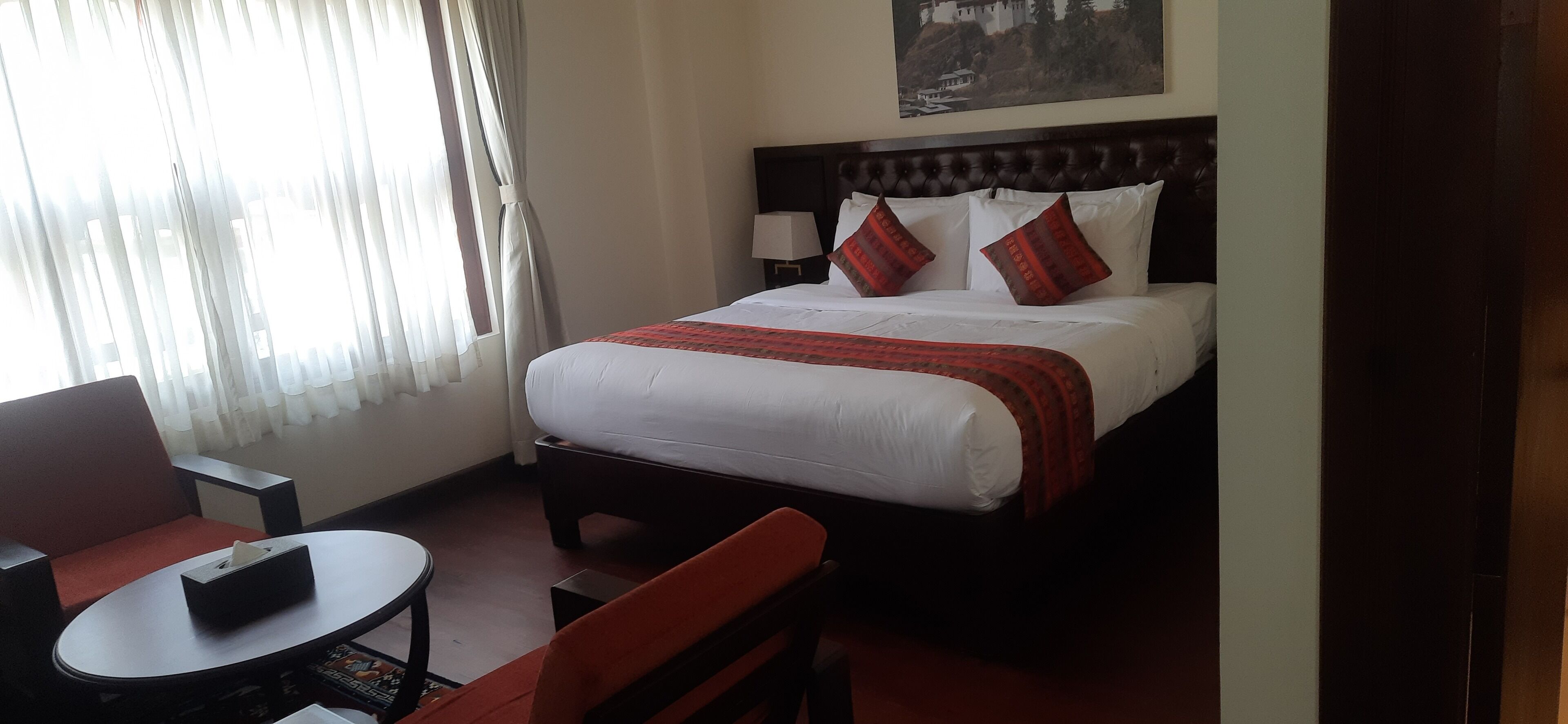 A hotel room with a bed, a small table, a chair, and a window with curtains.