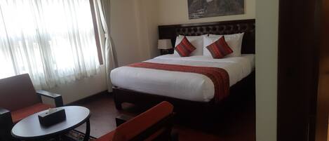 A hotel room with a bed, a small table, a chair, and a window with curtains.