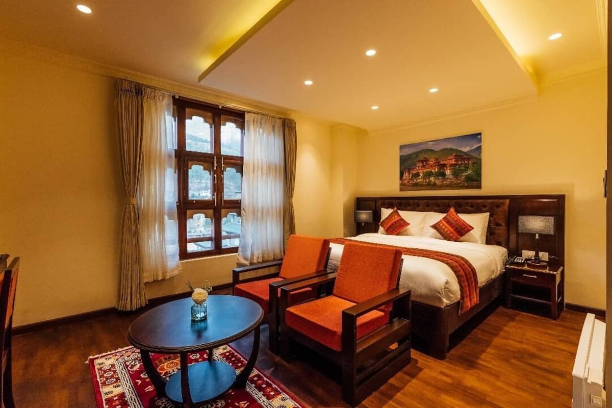 A hotel room with a large bed, two chairs, a small table, and a painting on the wall.